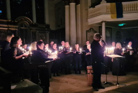 Jeffrey Skidmore talking to the audience in front of Ex Cathedra, who are standing in a semi-circle holding candles