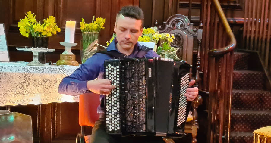 Miloš seated and playing his accordion. His eyes are closed as he concentrates on the music.