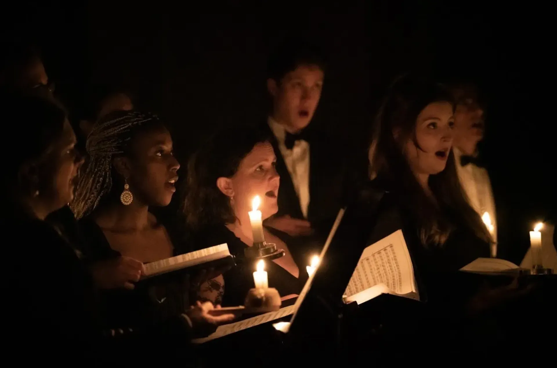 A close up of some of Ex Cathedra's singers in concert, their faces and music lit by lighted candles.